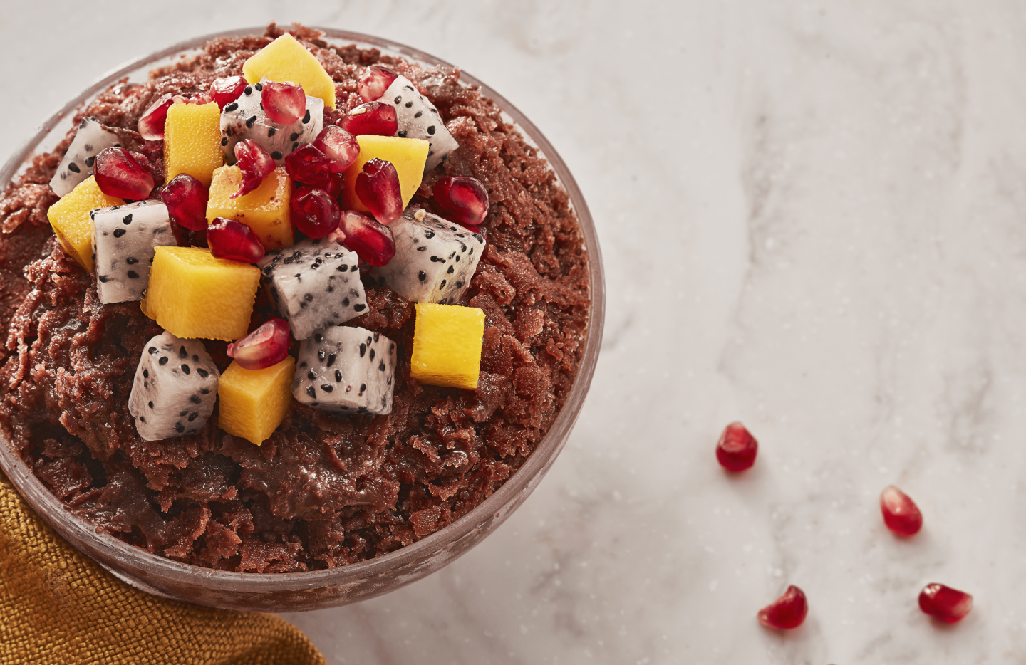 Shaved ice dessert with chopped fruit, pomegranate seeds and other toppings